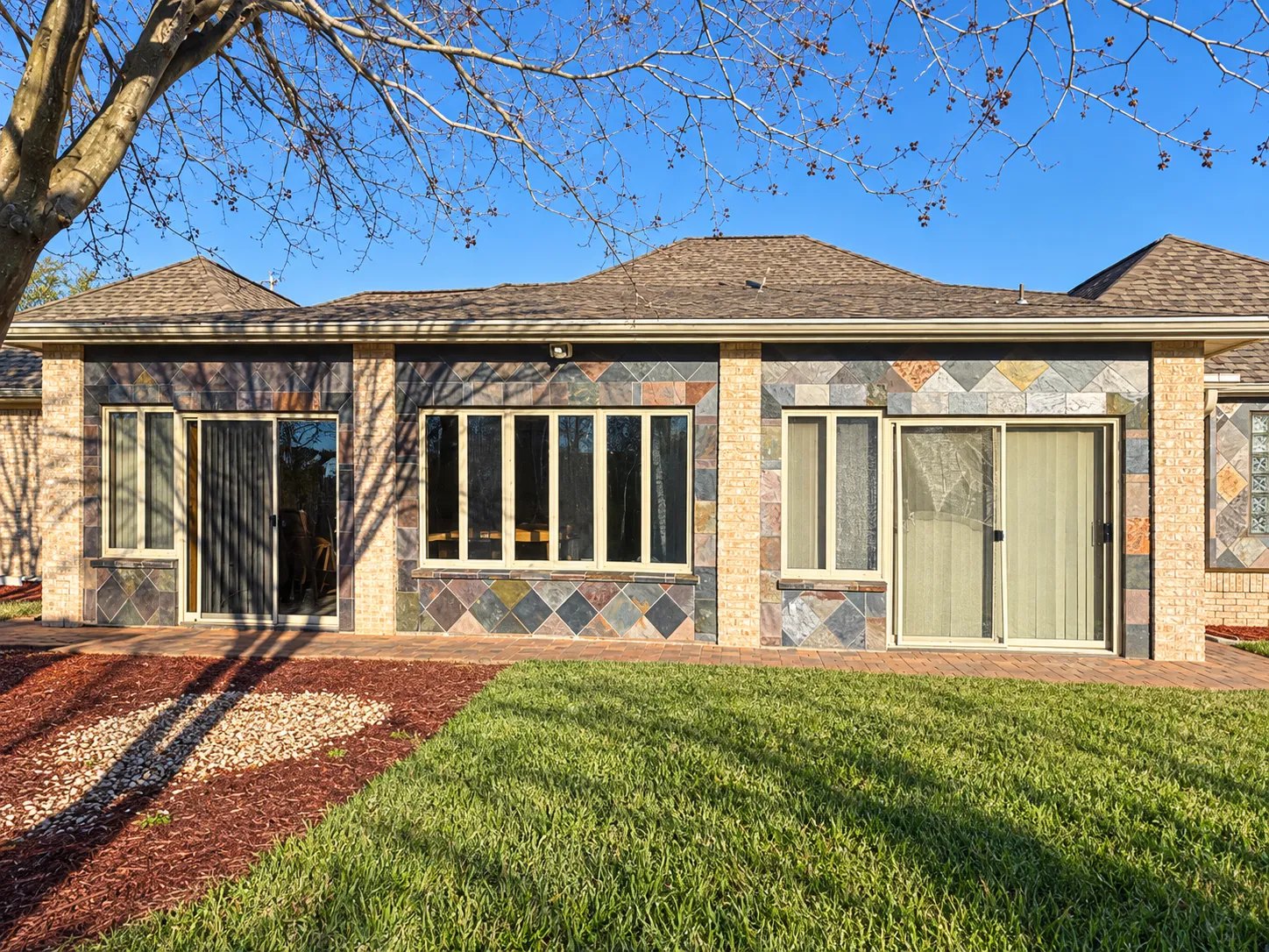 Back of the house before renovation: stone-accent wall with sliding doors, brick pavers and no patio cover